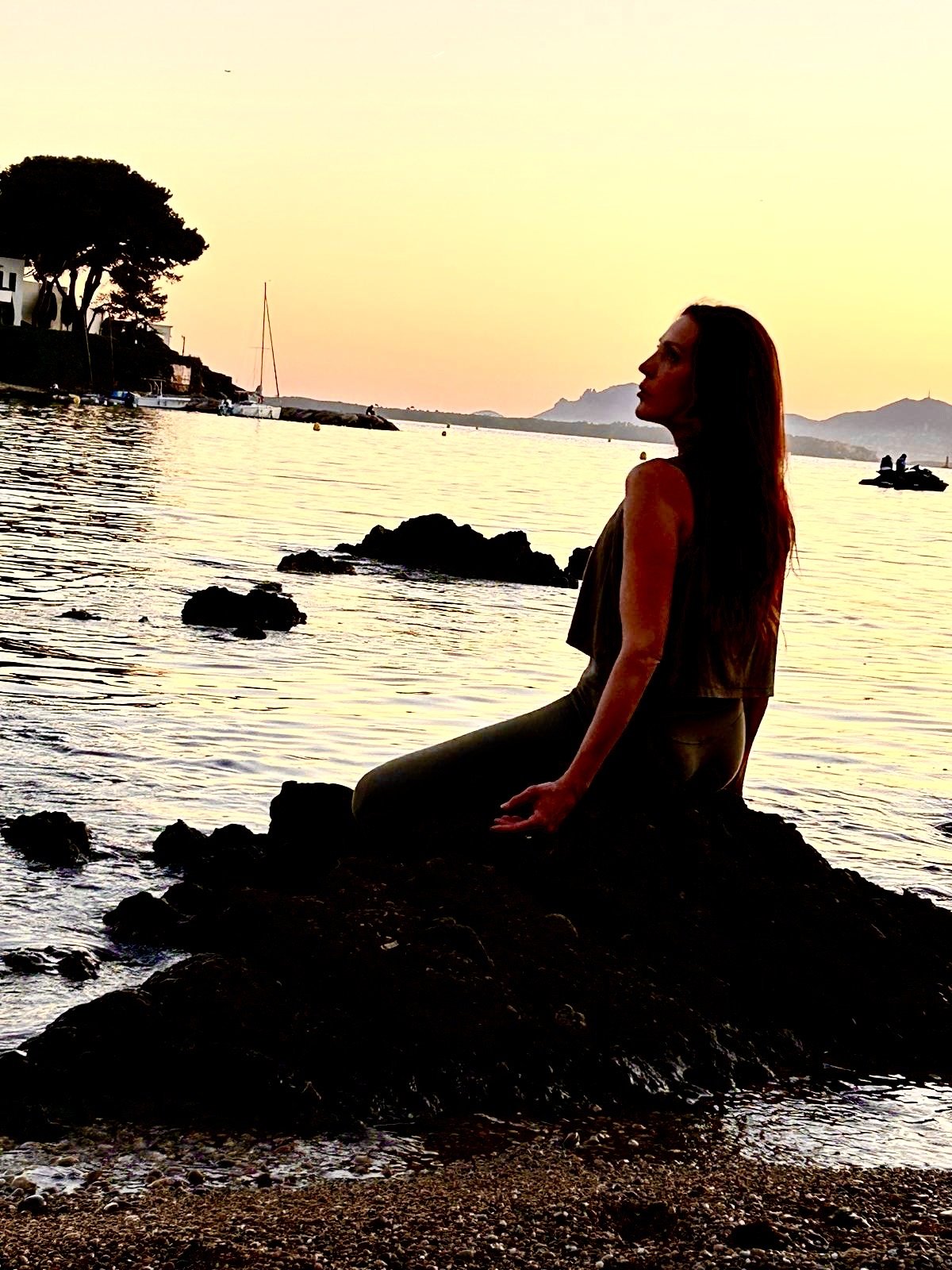 Une silhouette de profil, assise au bord de la mer à la lumière du soir.